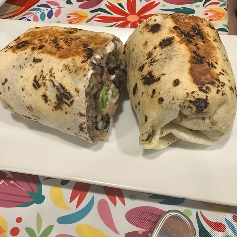 Two large, grilled burritos, one cut in half to show the meat and vegetable filling.