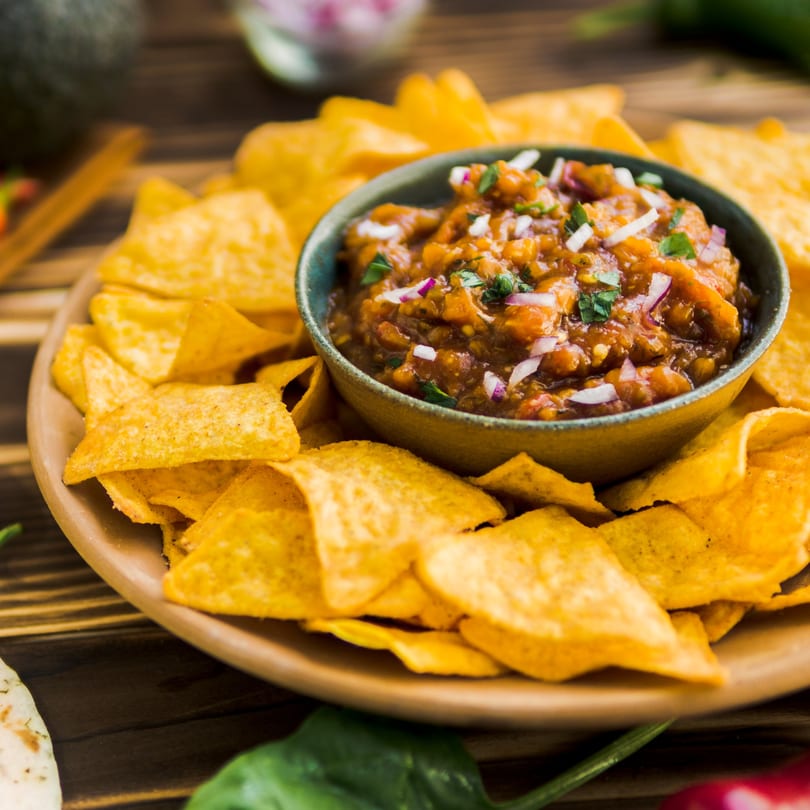 A bowl of Chi Chi's Tacoria salsa with red onions and cilantro, surrounded by tortilla chips.