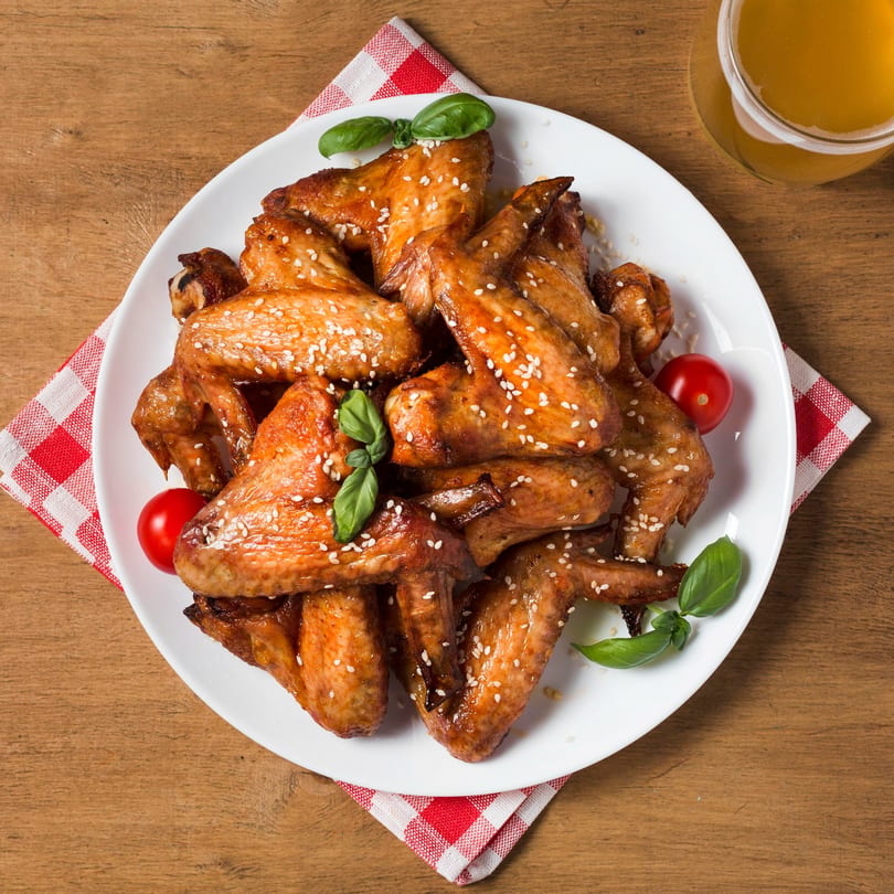 A plate of sesame chicken wings with basil and cherry tomatoes, next to a glass of beer.