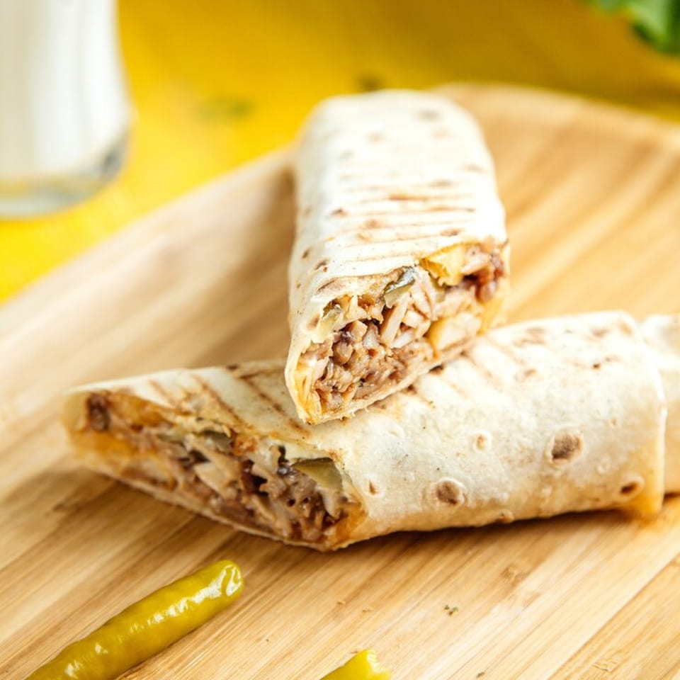 Two grilled Chi Chi's Tacoria burritos with meat and vegetables, on a wooden board.