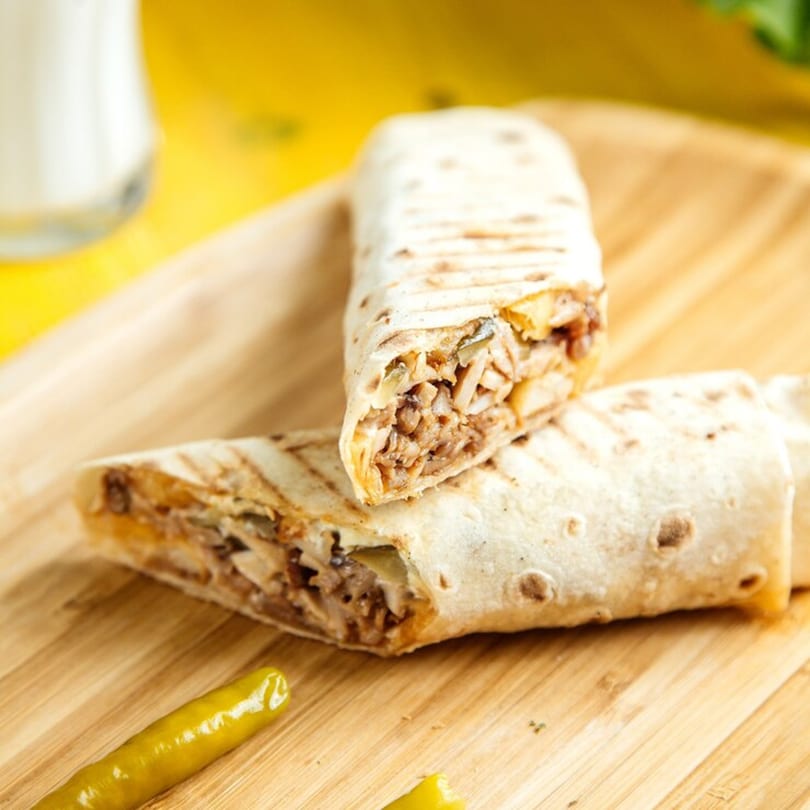 Two grilled Chi Chi's Tacoria burritos with meat and vegetables, on a wooden board.